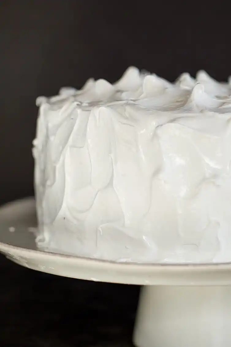 A devil's food cake covered in seven minute frosting on a cake stand.