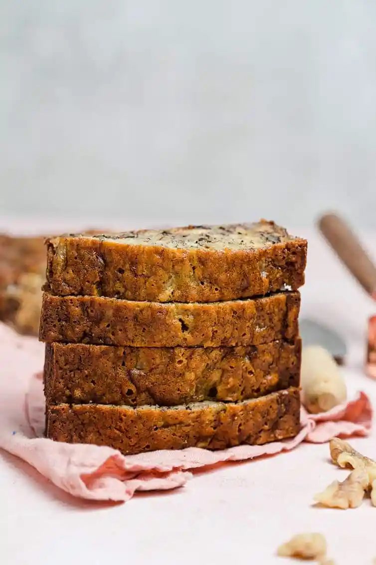 A stack of banana nut bread slices on a pink tea towel.