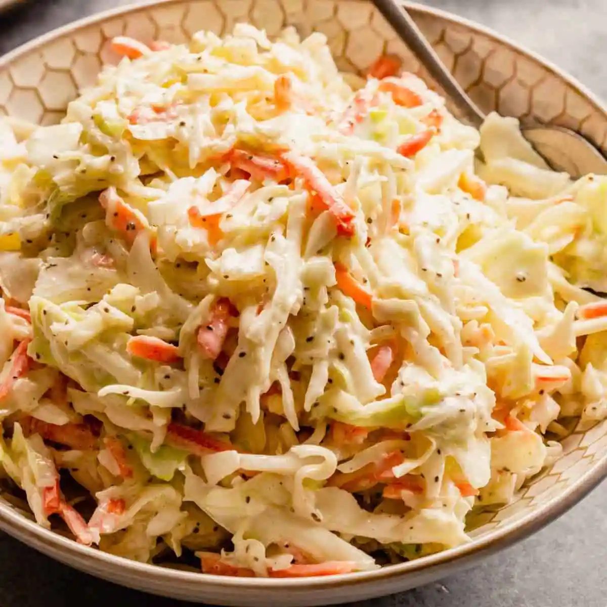 A white bowl with creamy from-scratch coleslaw and a silver spoon on the right side of the bowl.