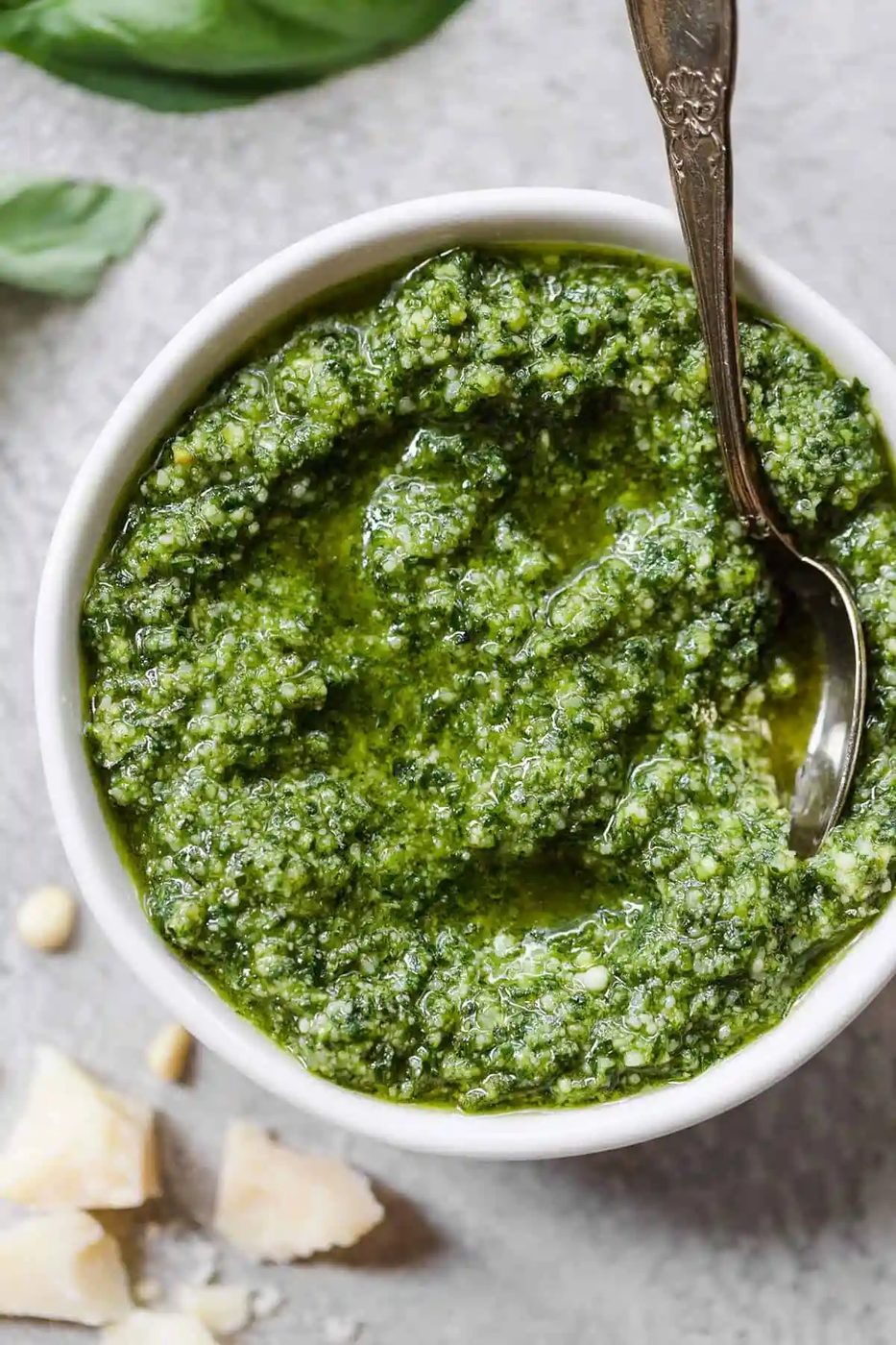 A white bowl with from-scratch pesto and a silver spoon in the right side of the bowl.