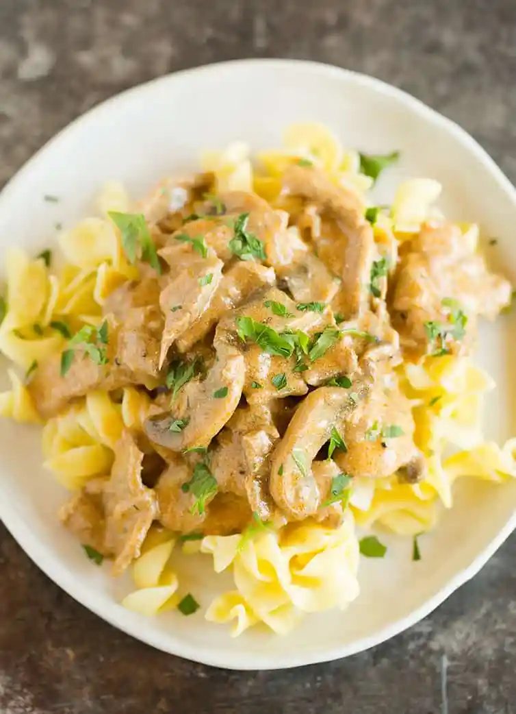 A plate of beef stroganoff over egg noodles.