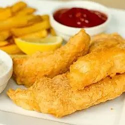 Beer battered cod and french fries on a white plate with lemon wedges, tartar sauce in a white bowl, and ketchup in a white bowl.