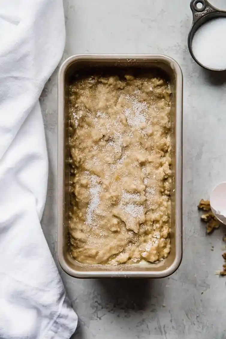 Banana bread batter in a loaf pan with sugar sprinkled on top.