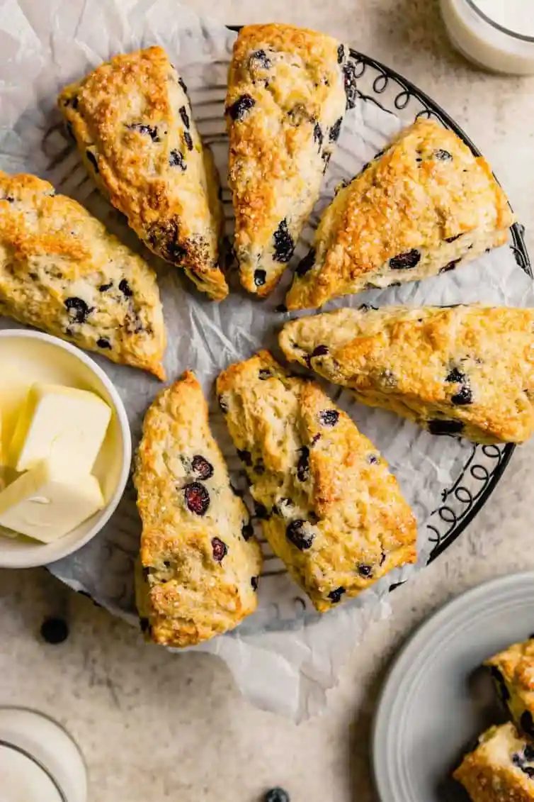A circular cooling rack with seven buttermilk scones and a small bowl with fresh sliced butter.