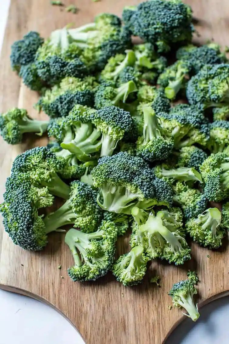 Broccoli florets on a wooden cutting board.