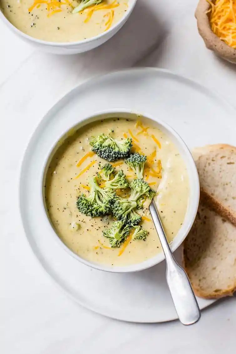 A bowl of broccoli cheese soup with bread on the side.
