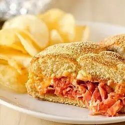 Chipotle ham BBQ sandwich cut in half with potato chips on a white plate.