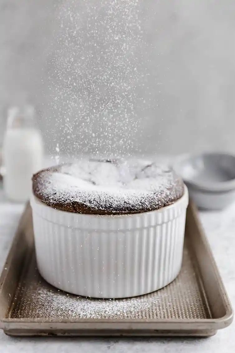 A chocolate souffle with powdered sugar being sprinkled on top.