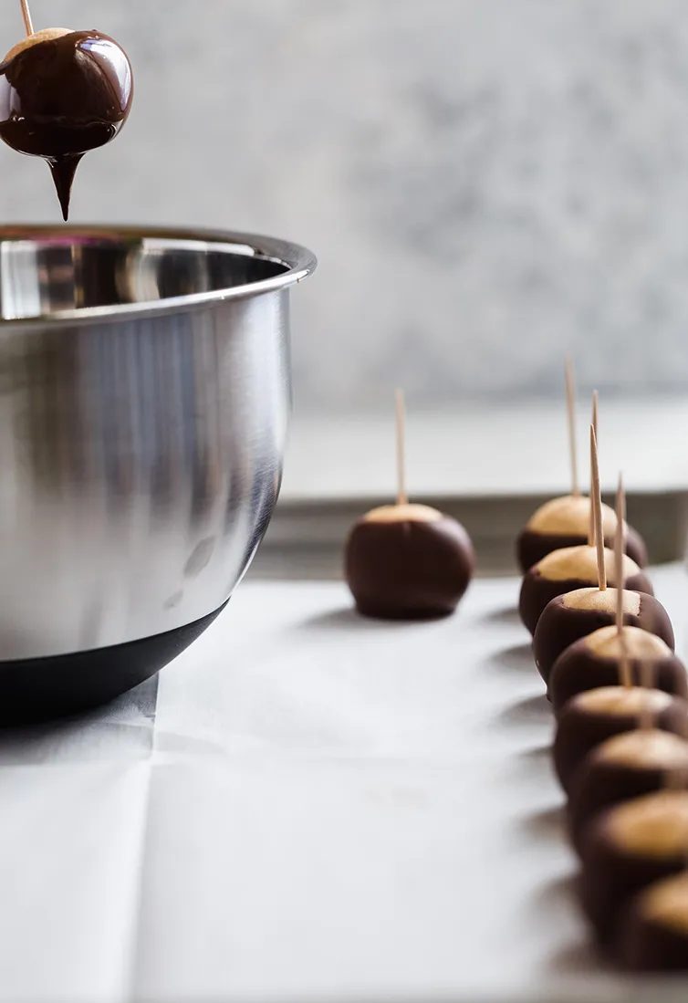 Dipping a buckeye into chocolate with finished ones on a pan.