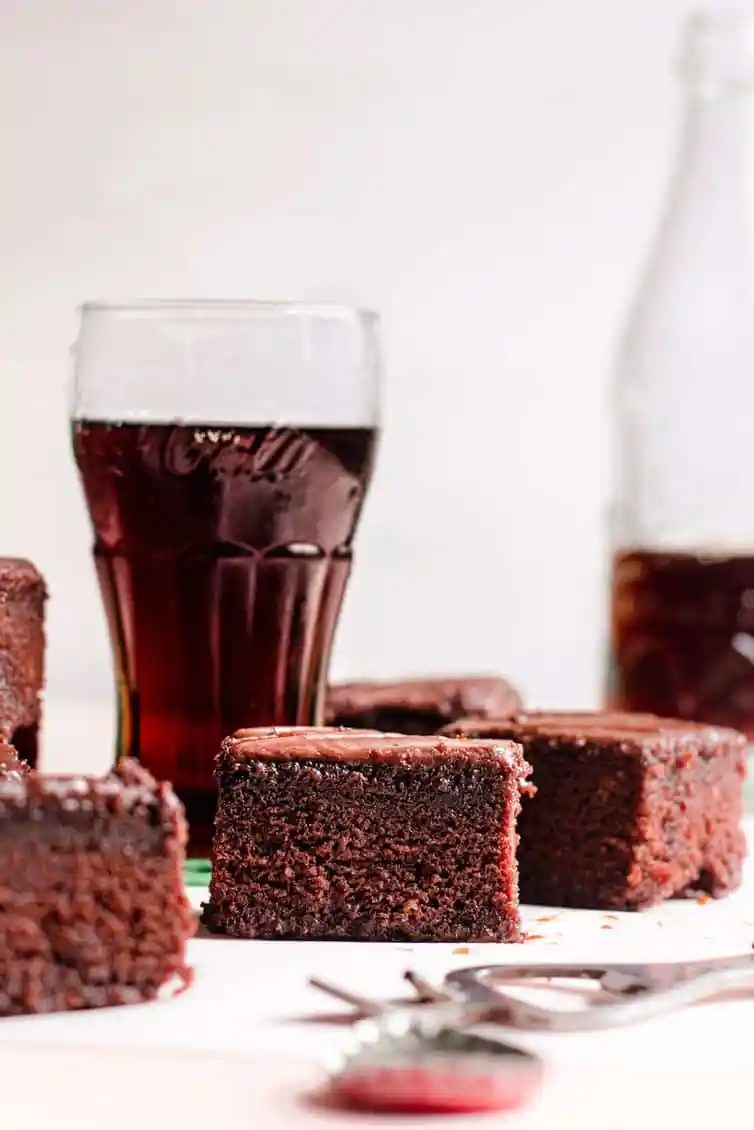 Pieces of chocolate cake in front of glasses of Coca Cola.