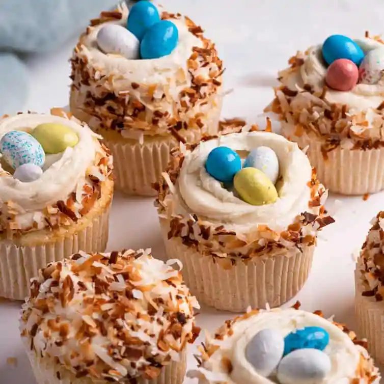 A square photo of coconut cupcakes topped with coconut frosting and toasted coconut.