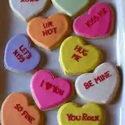Heart shaped sugar cookies decorated like conversation hearts on a white plate.