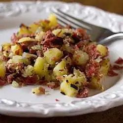 Serving of corned beef hash on a white plate with a fork.