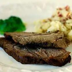 Serving of roast lamb on a white plate with potatoes and vegetables.