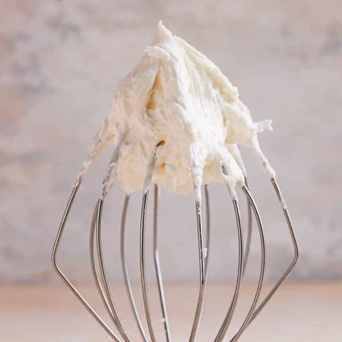 A square photo of vanilla buttercream frosting on a wire whisk.