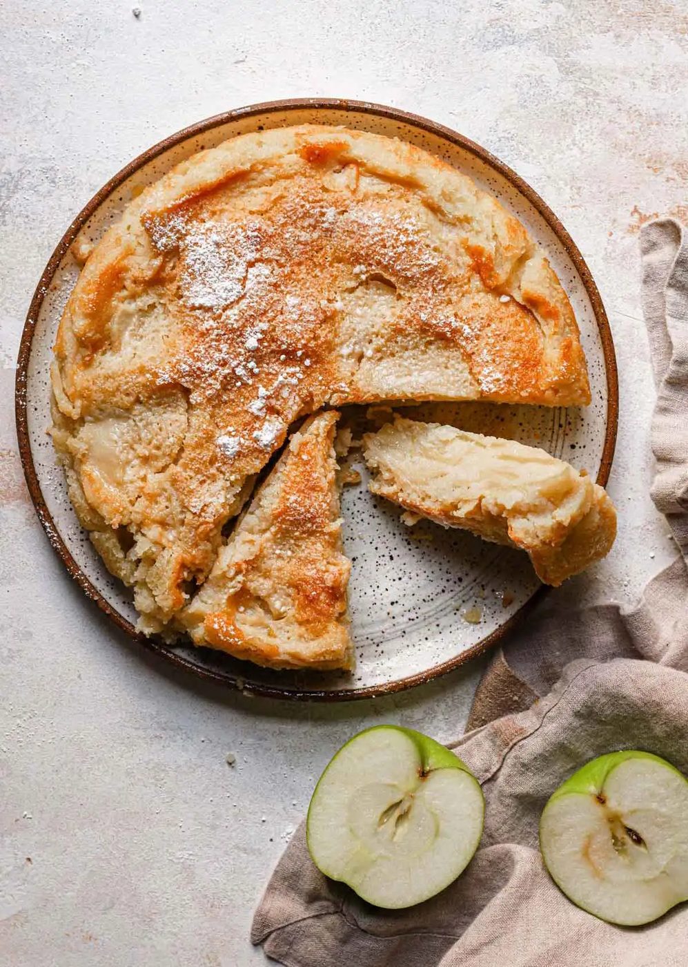 Overhead photo of French apple cake on a serving plate, with one slice cut away and on its side.