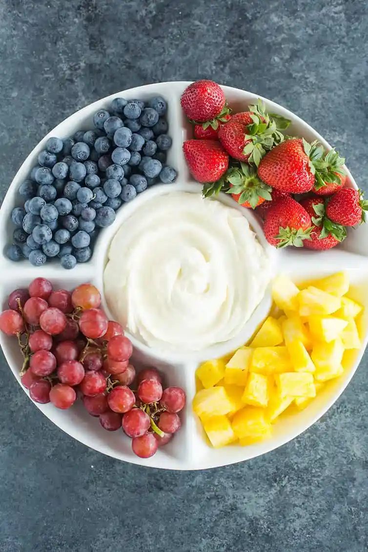 A platter of blueberries, strawberries, grapes and pineapple with fruit dip in the middle.