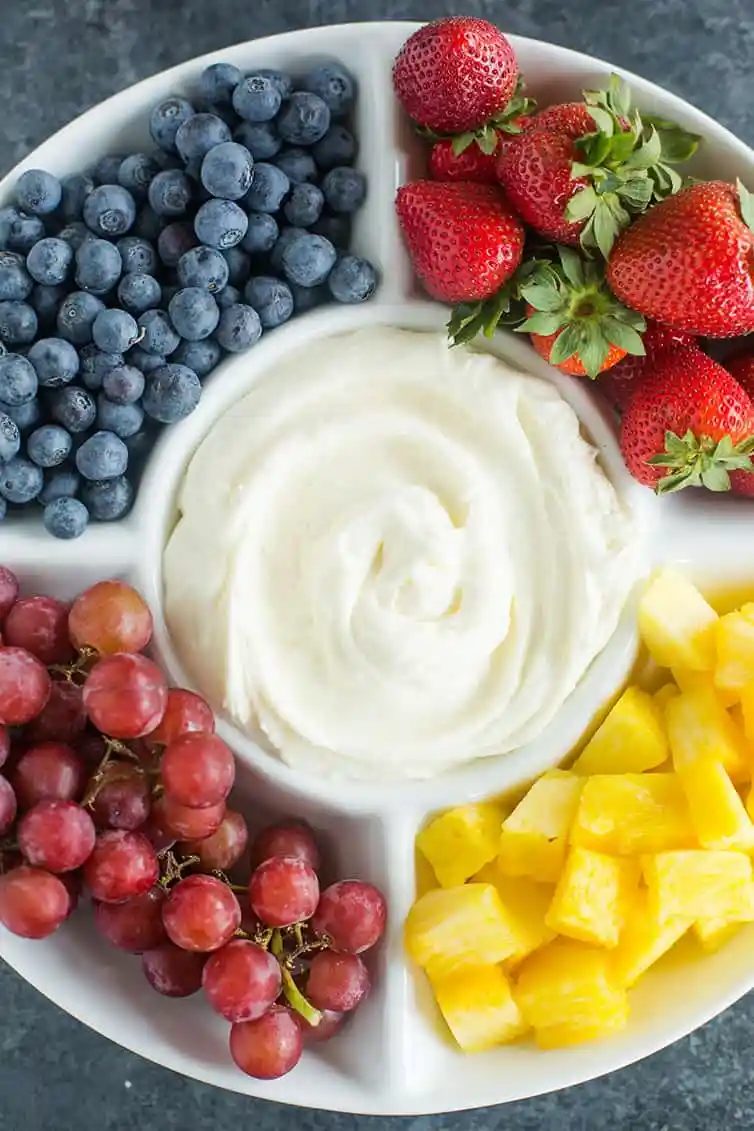 A platter of fruit dip with blueberries, strawberries, grapes and pineapple.