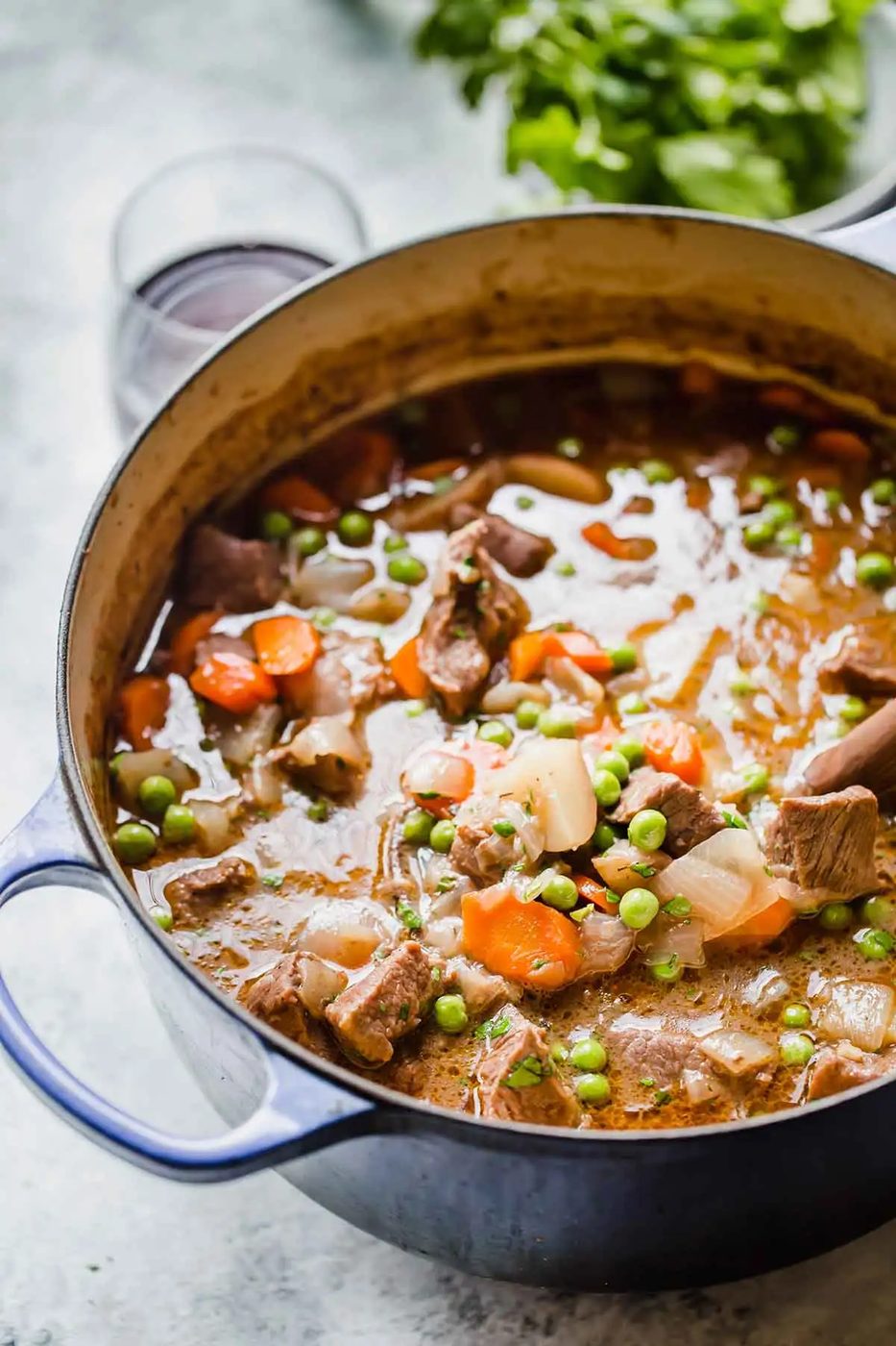 Beef stew in a pot on a grey counter with a glass of red wine in the background.