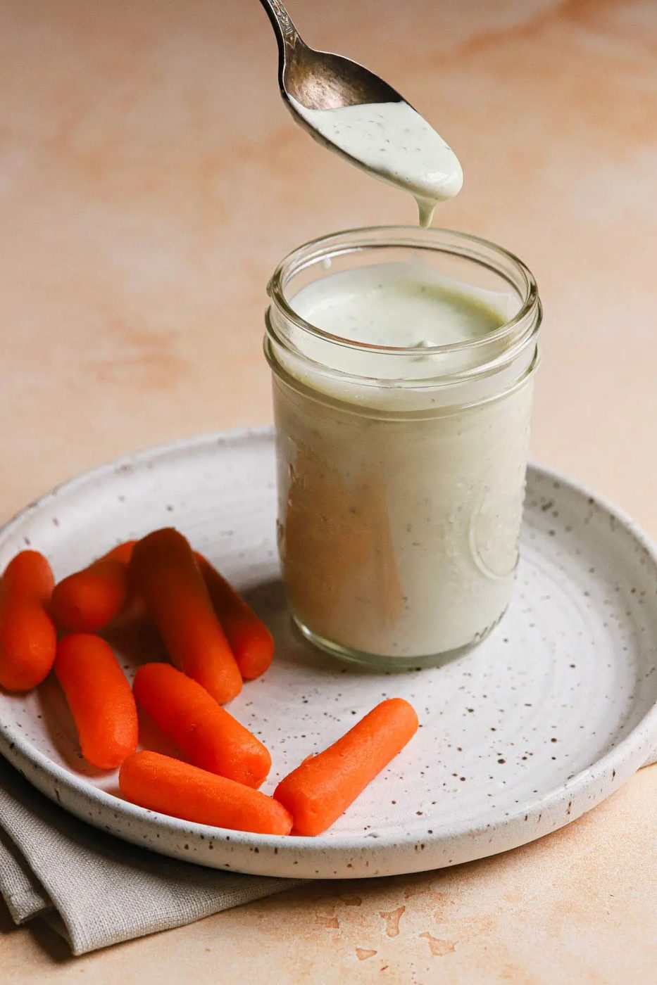 Spoon dipped into jar of from-scratch ranch dressing on a plate with baby carrots.