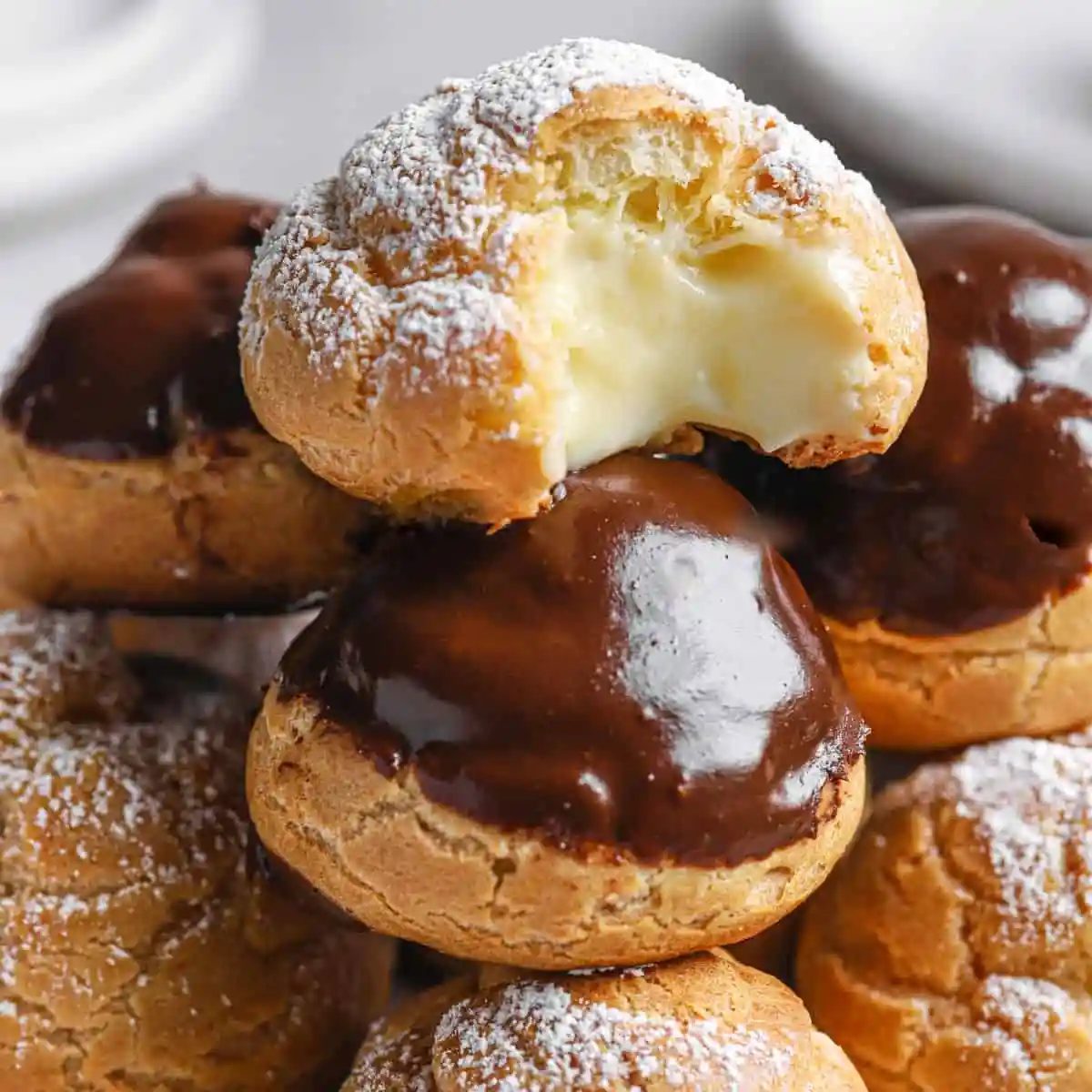 A close up of the top of a tower of cream puffs that has one cream puff on top with a missing bite.