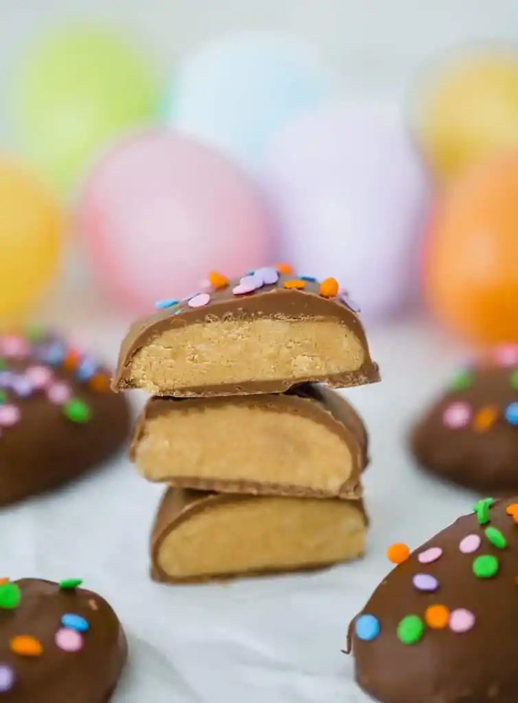 Peanut butter eggs, cut in half and stacked with Easter eggs in the background.
