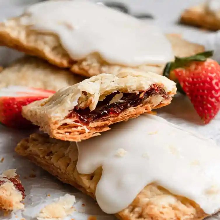 Half of a strawberry pop tart on top of iced from-scratch pop tarts on a piece of parchment paper.