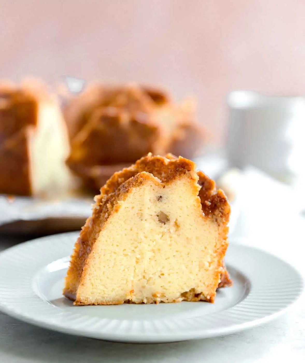 Slice of rum cake on a white plate with the whole cake in the background.