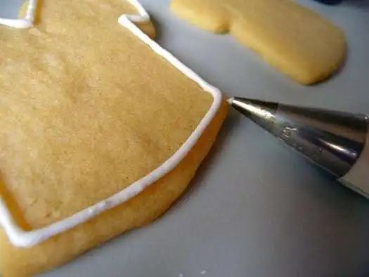 Using a piping tip to pipe a border of royal icing onto a sugar cookie.