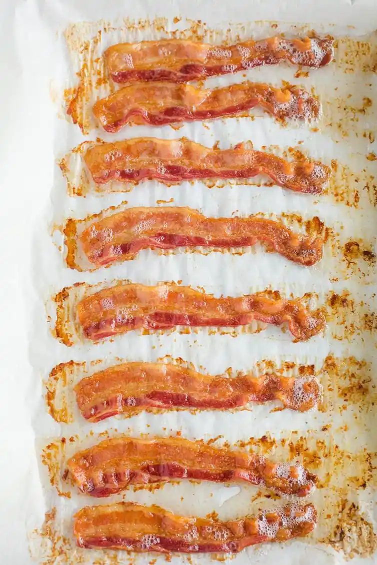 Freshly cooked oven baked bacon on a parchment-lined baking sheet.