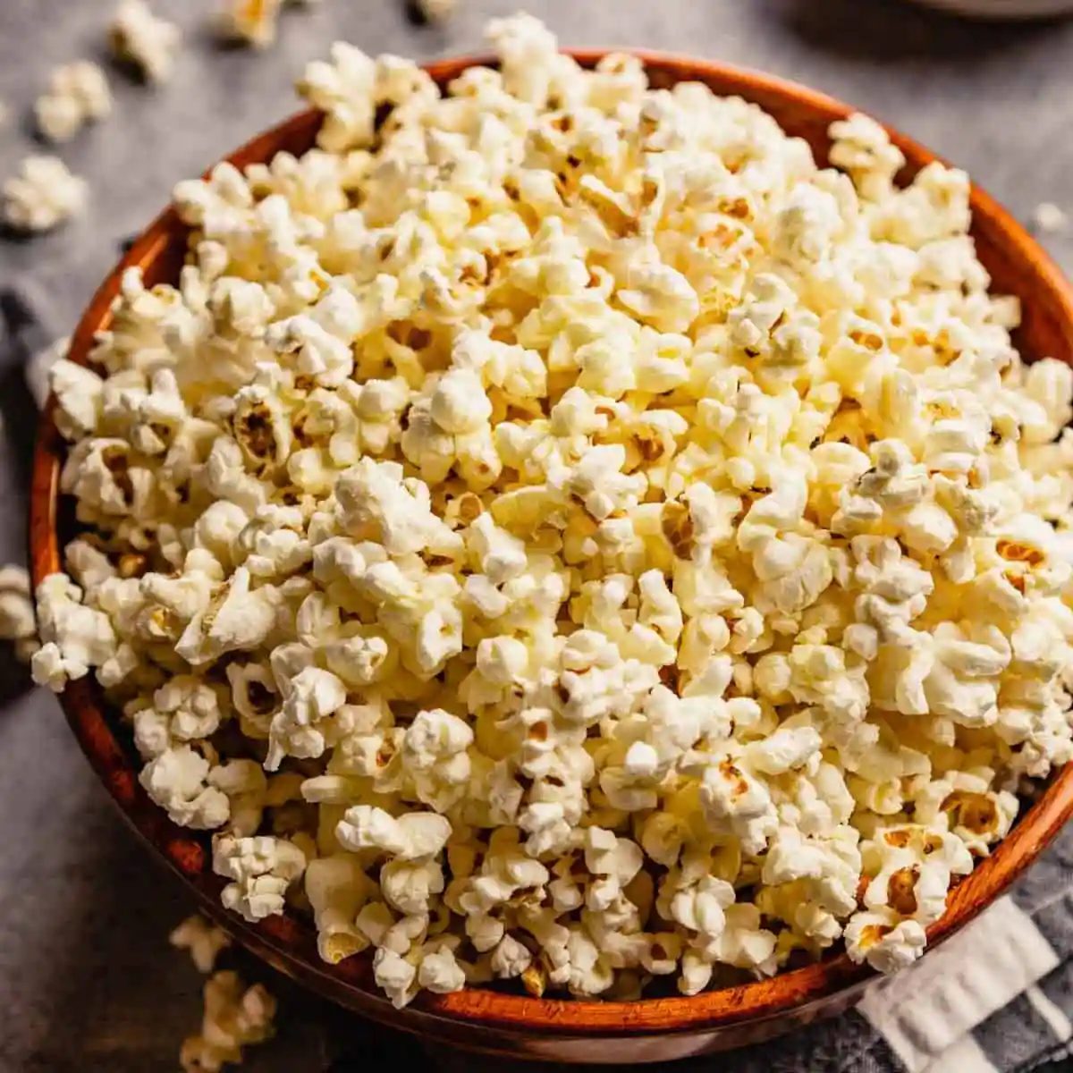 A brown bowl with fresh, from-scratch popcorn and some pieces of popcorn scattered on the counter.