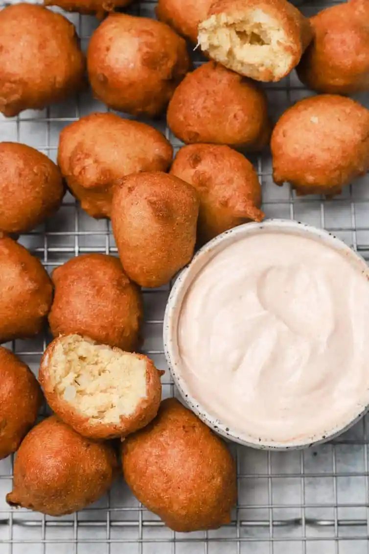 Hush puppies on wire rack with bowl of dipping sauce.
