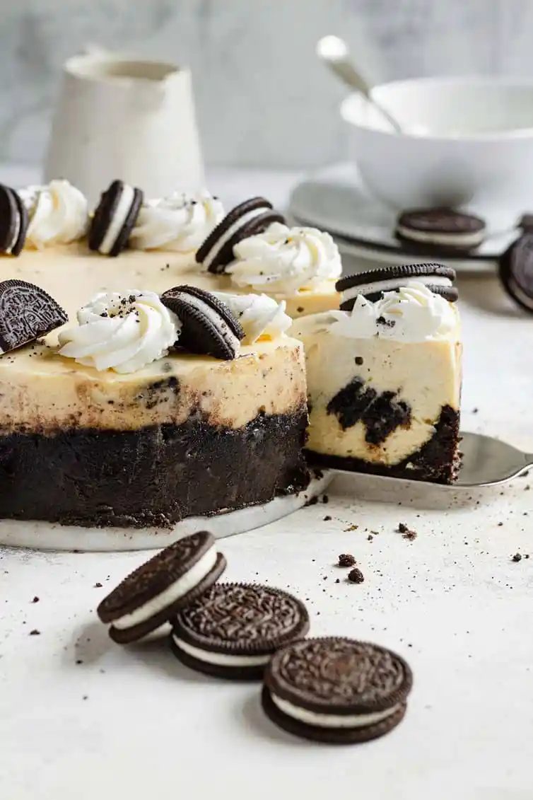 Oreo cheesecake with a slice coming out and Oreo cookies on the counter.