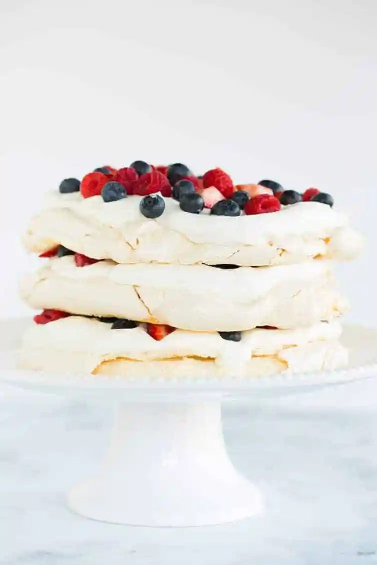 Three layers of pavlova filled and topped with whipped cream and berries.
