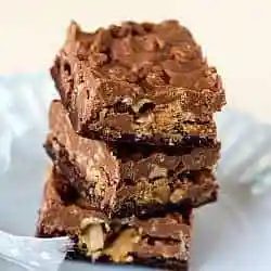 Stack of 3 peanut butter cup crunch brownie bars on a white plate.