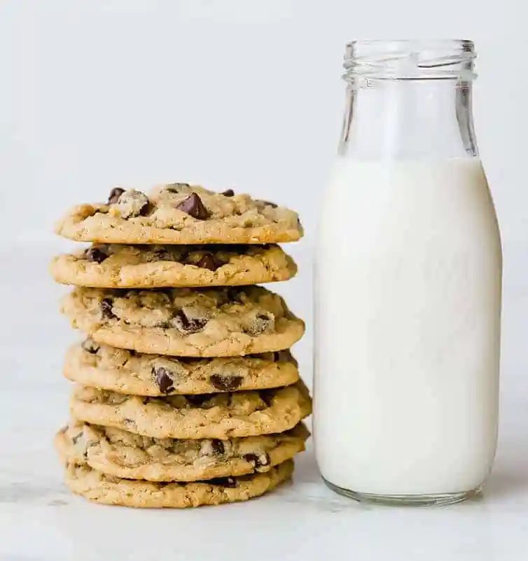 A stack of peanut butter-oatmeal chocolate chip cookies next to a glass bottle of milk.