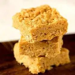 Stack of 3 peanut butter and white chocolate Rice Krispies treats on a wood board.