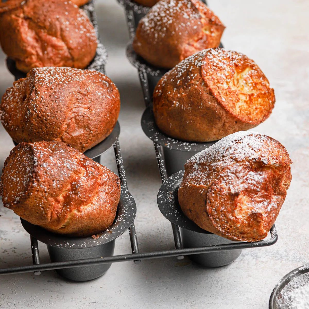 Golden brown baked breakfast popovers in a grey popover baking pan dusted with powdered sugar