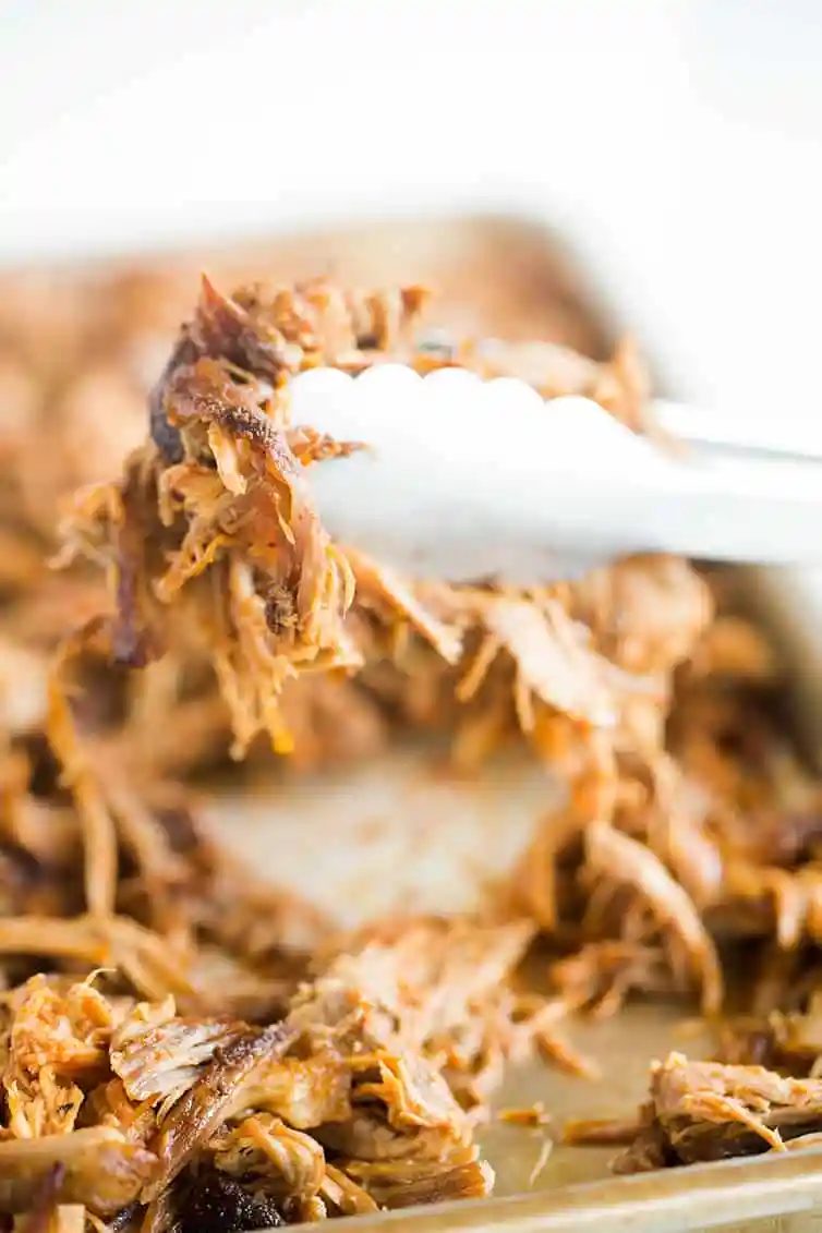 Pulled pork being picked up with large tongs.