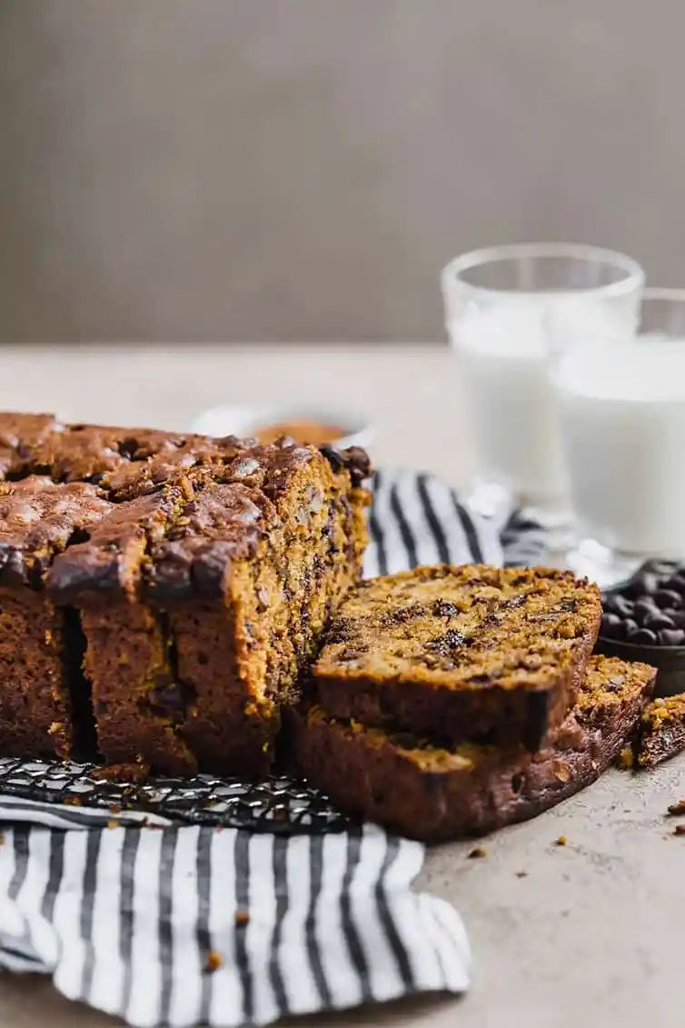 A loaf of pumpkin bread sliced with two glasses of milk.