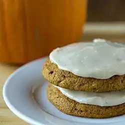 Stack of 2 pumpkin cookies topped with brown butter icing on a white plate.
