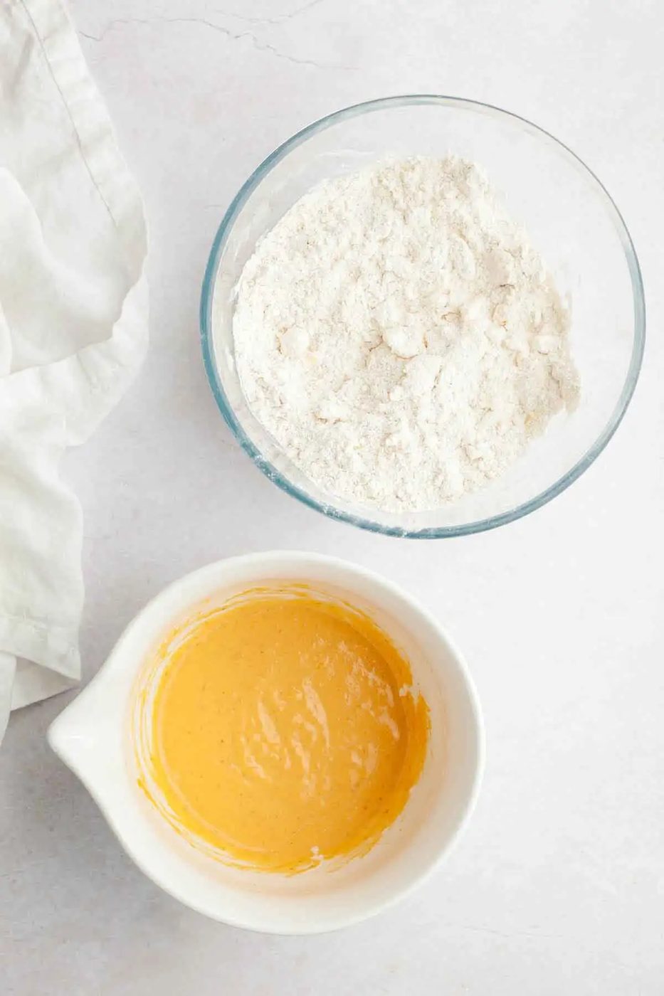Two bowls, one with dry ingredients and cubed butter, the other with wet ingredients for pumpkin scones.