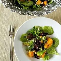 Overhead image of a serving of roasted butternut squash salad with cider vinaigrette in a white bowl with a fork.