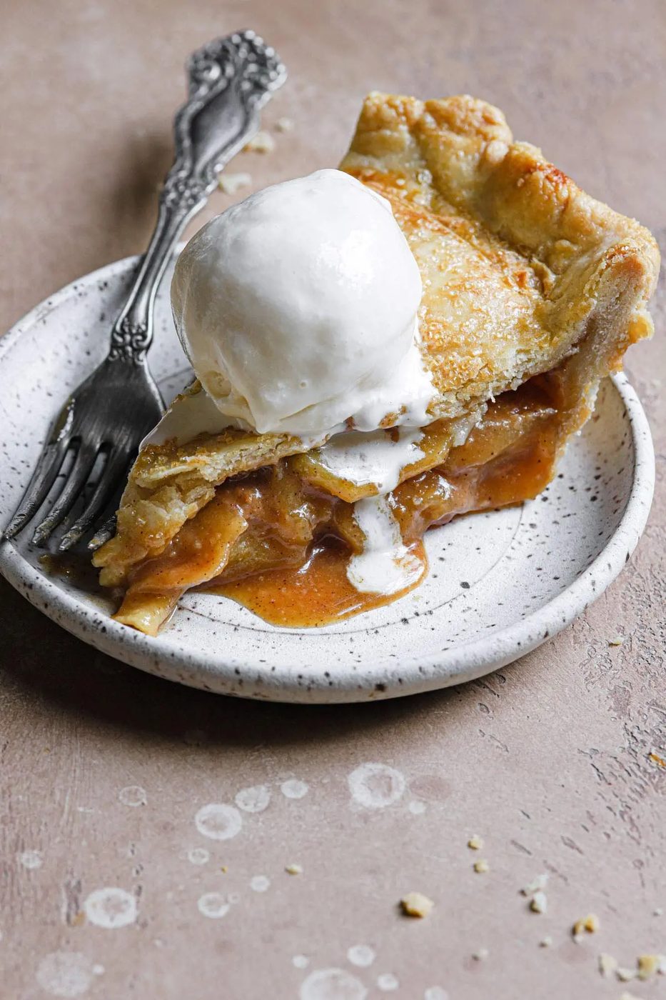 a slice of this salted caramel apple pie served on a stoneware plate with vanilla ice cream