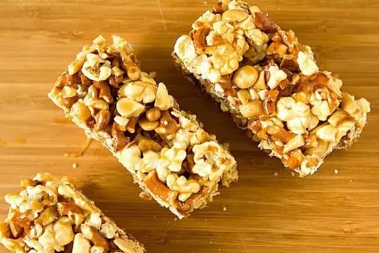 Overhead image of salted caramel popcorn, pretzel, and peanut bars on a wood board.