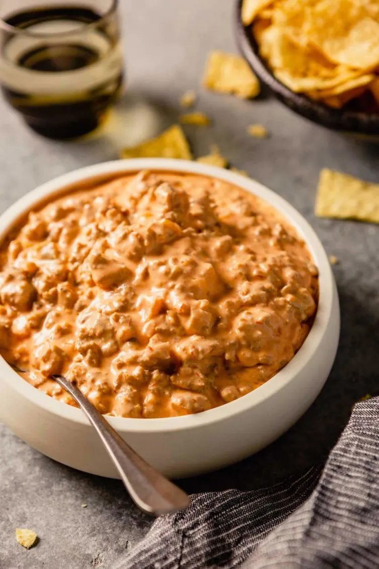 A white bowl filled with creamy sausage dip with a spoon to the left and chips in the back.