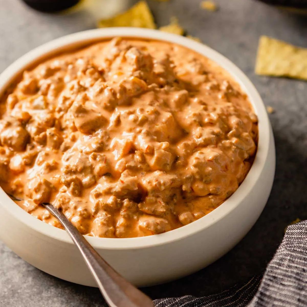 A top down photo of a white bowl with creamy sausage dip with a silver spoon on the left side on the bowl.