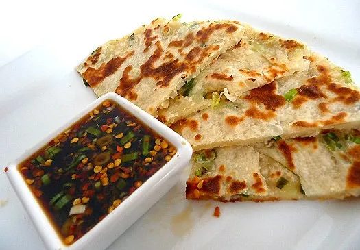 Scallion pancakes with a ginger dipping sauce on a white plate.