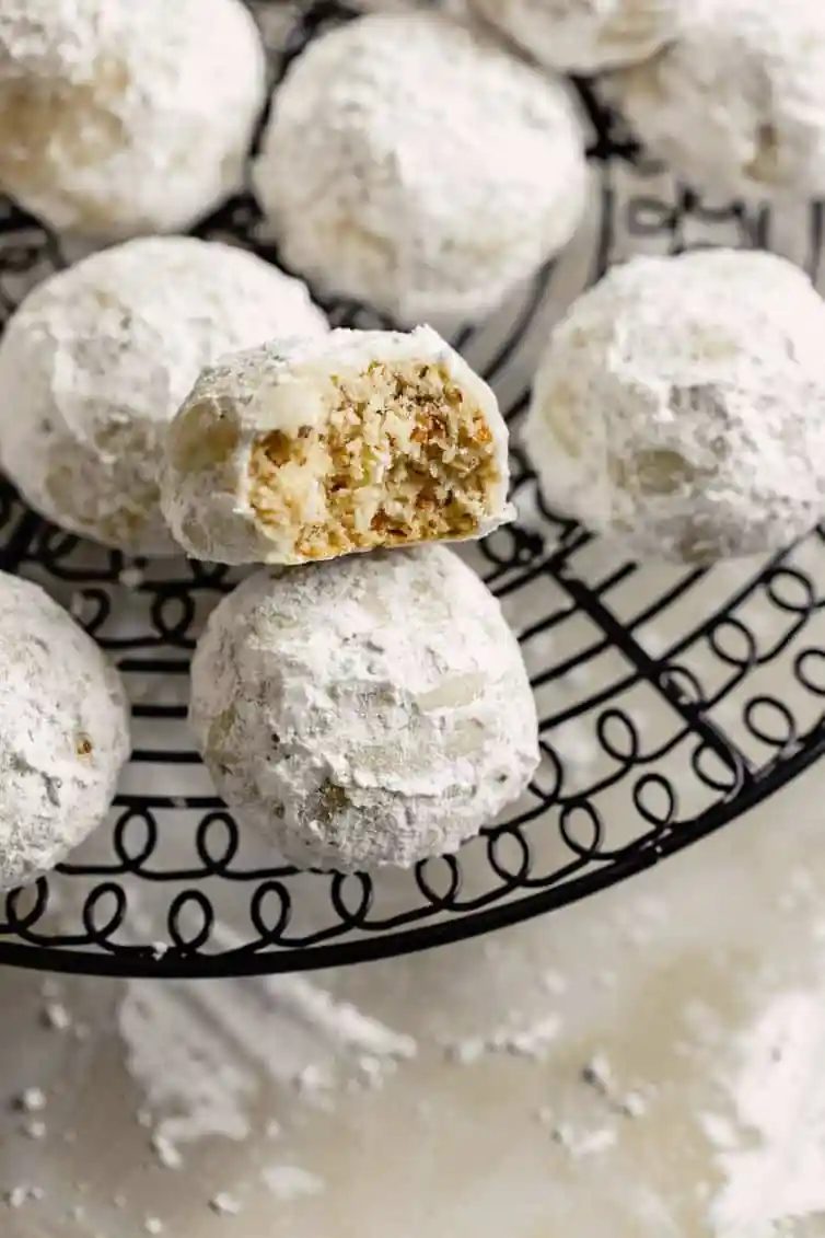 Snowball cookies on a wire rack with one bitten in half.