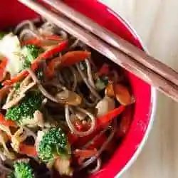 Soba noodle stir fry in a red bowl with chopsticks.